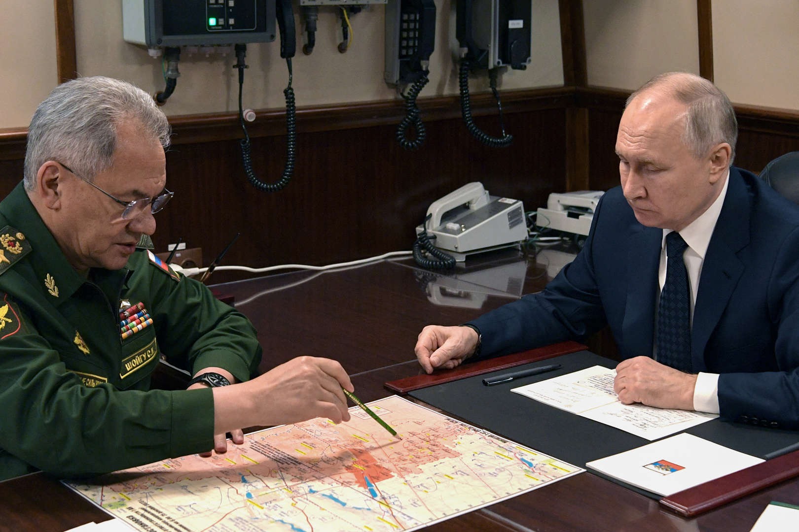 alt=Two military men discussing strategies over maps at a table.