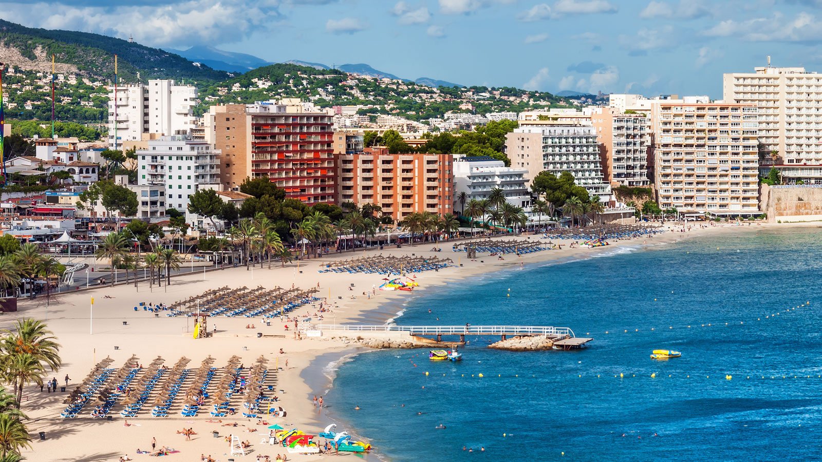 alt=Alt text: "City beach in Majorca with towering buildings and a serene blue ocean."