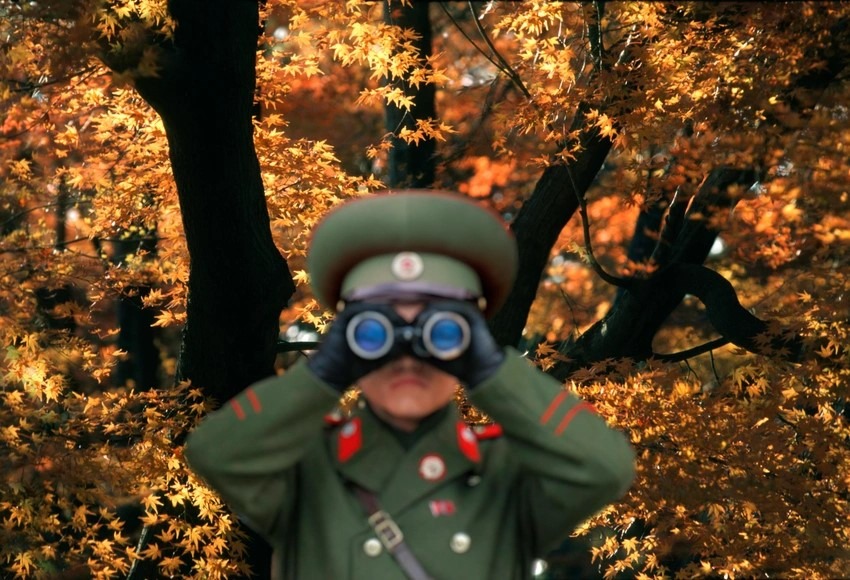 alt=A soldier in uniform using binoculars to observe surroundings.