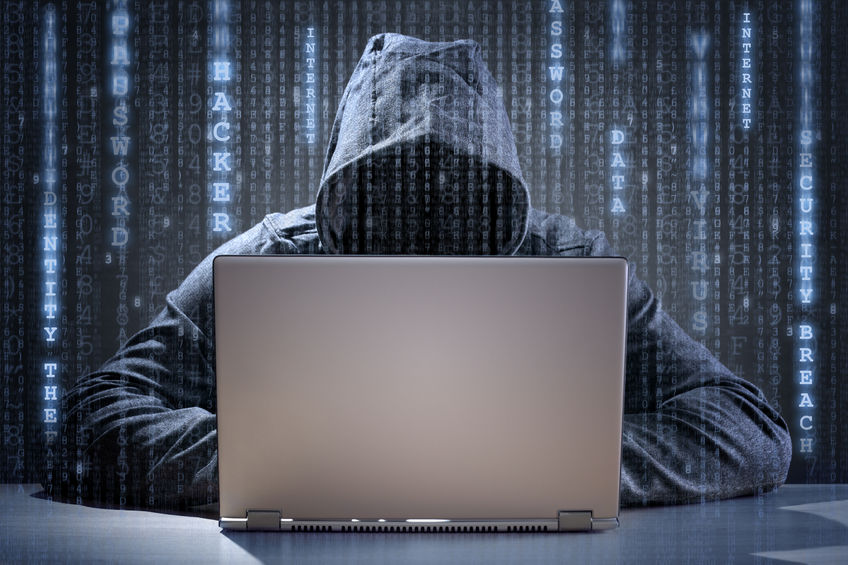 alt= Individual wearing hoodie, seated at laptop - potential hacker.