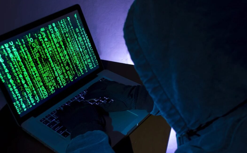 alt=A person wearing a hoodie is focused on using a laptop computer in a casual setting.