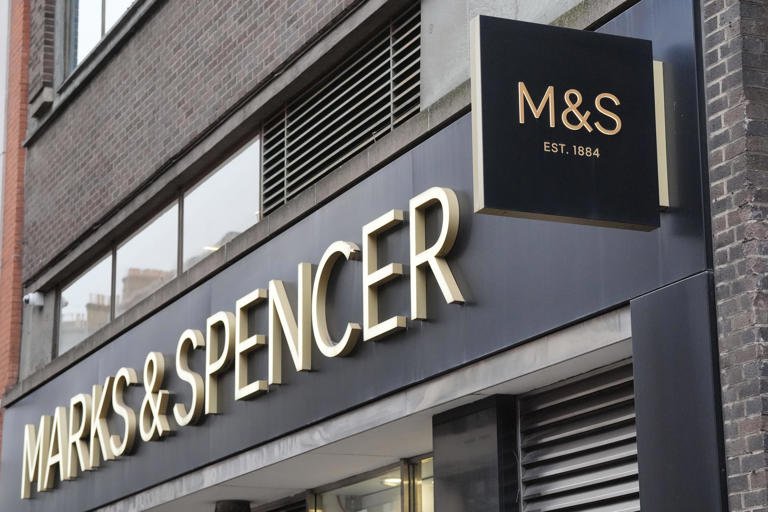 alt=Signage of Marks & Spencer, featuring the logo 'M&S' and the establishment year 'EST. 1884', on a city's storefront.