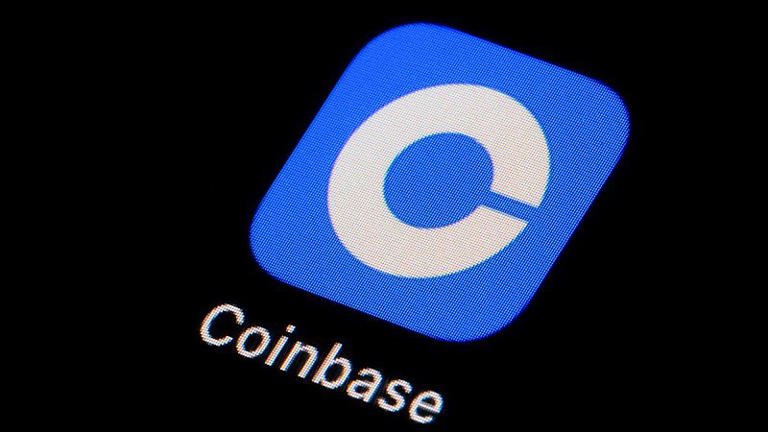 alt=Close-up of the Coinbase app icon on a dark screen, featuring a blue background with a white letter "C" and the word "Coinbase" below.