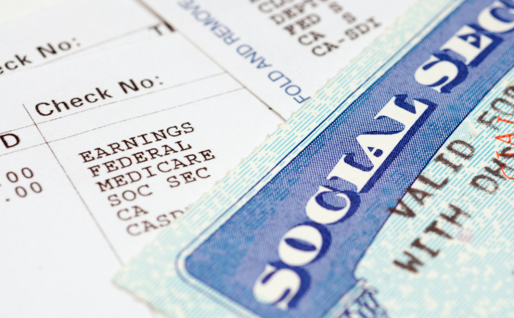 alt=Close-up of a Social Security card beside a paycheck showing earnings, federal and Medicare with check numbers visible.