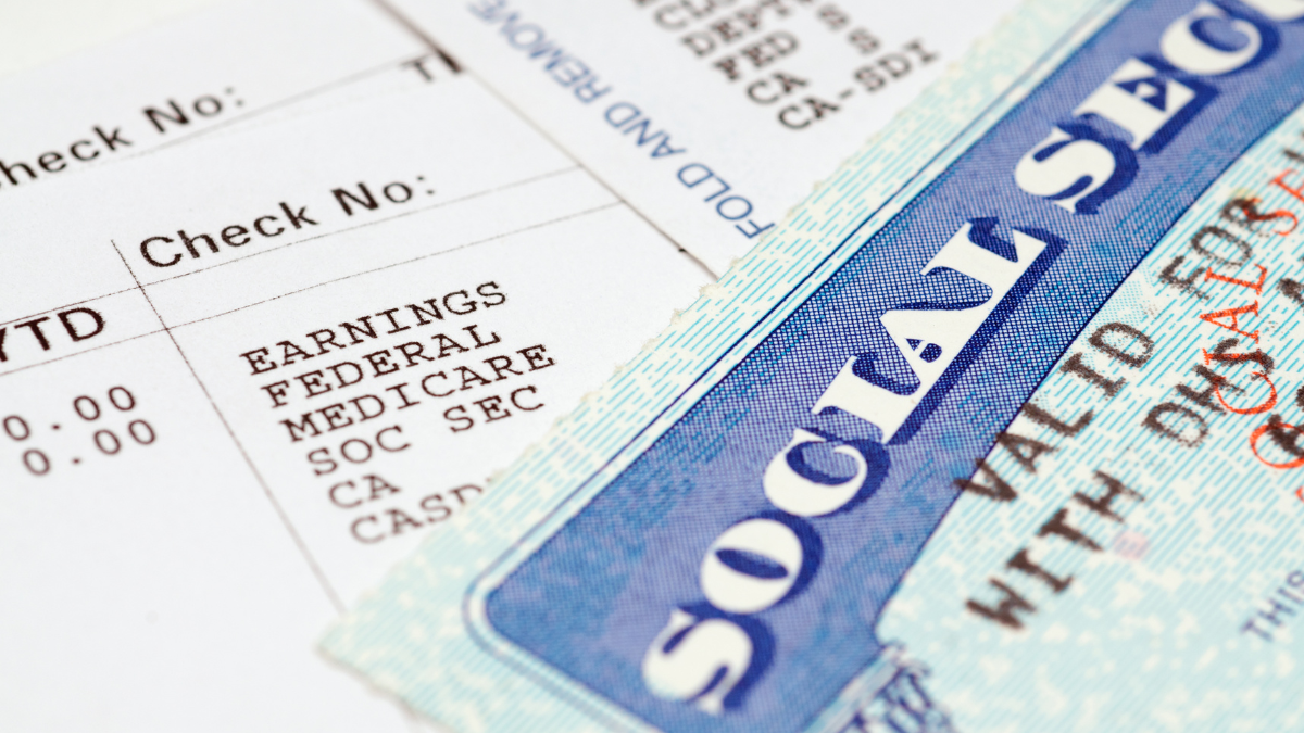 alt=Close-up of a Social Security card beside a paycheck showing earnings, federal and Medicare with check numbers visible.