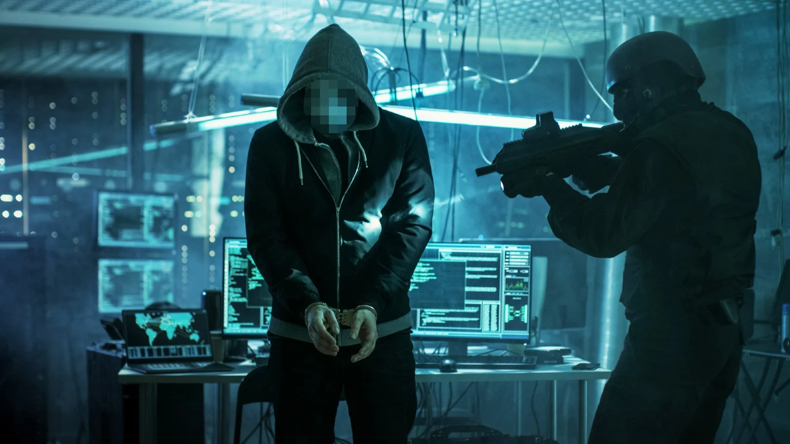 alt=A hooded figure stands with hands bound, while a tactical officer aims a weapon at them in a dimly lit, tech-filled room.