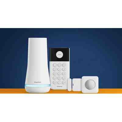 alt=A home security system featuring a white base station, keypad, and motion sensor, set against a blue background with an orange surface.