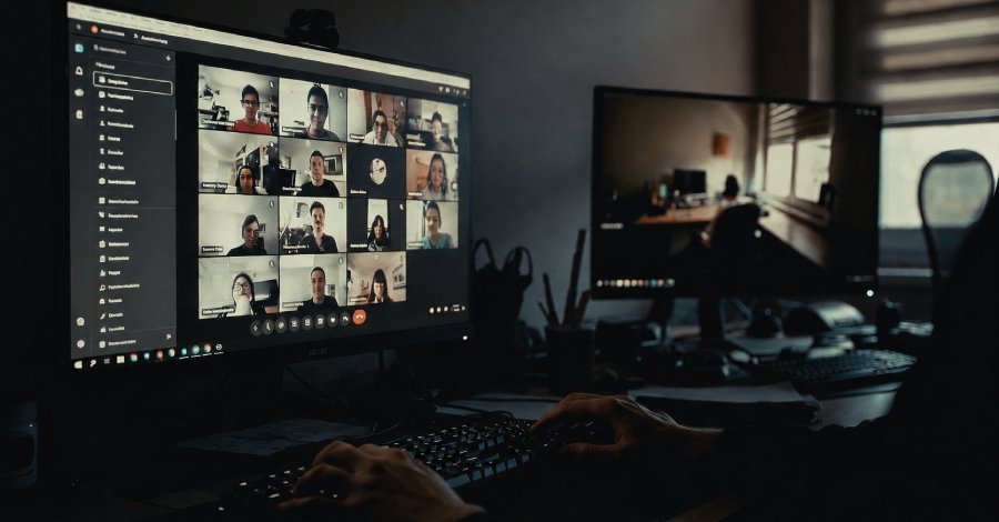 alt=Person attending a dark room virtual meeting with multiple participants displayed on a computer screen.