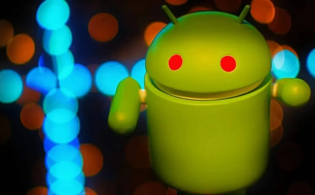 alt=Green Android figurine with glowing red eyes against a background of blurred blue and orange lights.